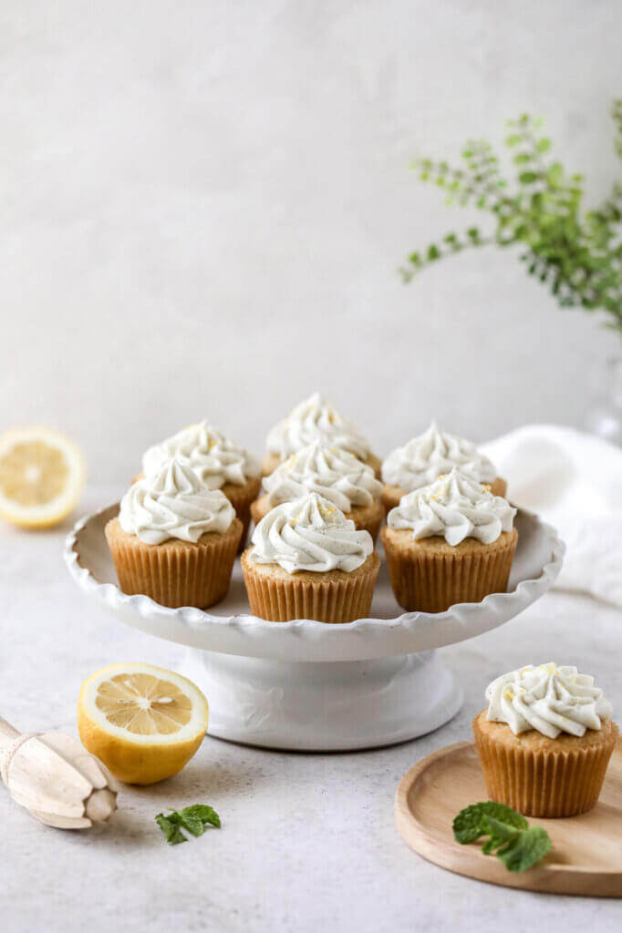 A cake stand with frosted cupcakes and lemons scattered around and one plate with a cupcake on it. 