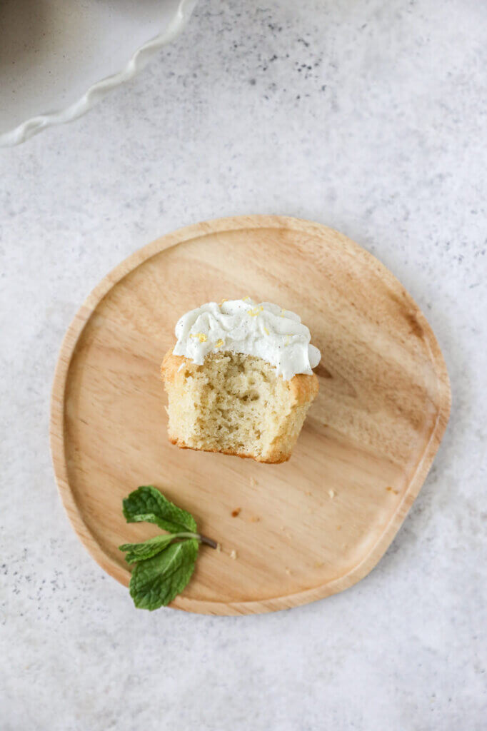 Top down view of a lemon cupcake on a plate with a bite taken out of it. 